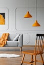 Chair in a living room interior with a wall molding, orange lamp and sofa. Real photo
