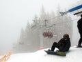 Chairlift with people in fog. Snowboarder sitting at the lift
