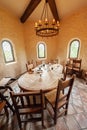 Chairs around an oblong wooden table in castle-like room..