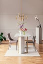 Chairs at table with flowers in modern dining room interior with gold lamp and carpet. Real photo