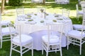 Chairs and table with white tablecloth decorated for the celebration of an outdoor banquet.