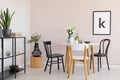 Chairs at wooden table with flowers in dining room interior with plants and poster. Real photo