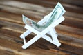 Chaise long or deck chair made of us dollar on wooden background, money for vacation concept