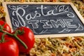 Chalk board sign Pasta Time on a wooden tabletop with raw farfalle, fresh tomatoes and black pepper Royalty Free Stock Photo