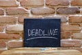 Chalk board with the word Deadline drown by hand on wooden table on brick wall background.