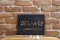 Chalk board with the word DELIVERY drown by hand on wooden table on brick wall background