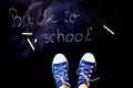 chalk and kid& x27;s feet on black background wearing sneakers - back to school concept