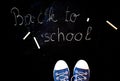 chalk and kid& x27;s feet on black background wearing sneakers - back to school concept