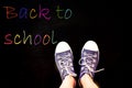 chalk and kid& x27;s feet on black background wearing sneakers - back to school concept