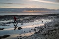 A chalk rock pool on a beach at sunset with reflections of the sky. A boy runs by with his reflection in the water