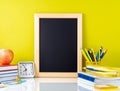 Chalkboard, apple and school supplies on white table by the yell