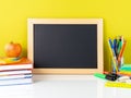 Chalkboard, apple and school supplies on white table by the yell