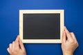 Chalkboard mock up. Female hands holding blackboard on a blue background, isolated. Copy space, flat lay. Business, education Royalty Free Stock Photo