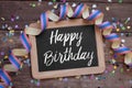 Chalkboard with paper streamer and confetti with happy birthday on old weathered wood background