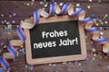 Chalkboard with paper streamers and confetti with the german words for happy new year - frohes neues jahr 2022 on wooden backgroun