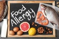 Chalkboard with phrase FOOD ALLERGY and different products on dark grey background