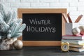 Chalkboard with phrase Winter Holidays, Christmas decor and stationery on black wooden table near white brick wall Royalty Free Stock Photo