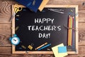 A chalkboard with the text happy teachers day written in it, school supplies and alarm clock on a rustic wooden table Royalty Free Stock Photo