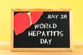 Chalkboard with text World Hepatitis Day. June 28th. Liver on a wooden table against a yellow wall background.