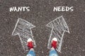 Chalky arrows Wants and Needs with feet in red sneakers from above standing on asphalt. Royalty Free Stock Photo