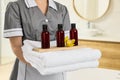 Chambermaid holding fresh towels with flower and shampoo bottles in hotel bathroom, closeup Royalty Free Stock Photo