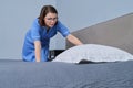 Chambermaid making guest bed in hotel bedroom, placing pillow