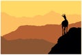 A chamois stands on top of a hill with mountains in the background. Black silhouette with brown and orange background.