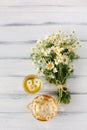 Chamomile bouquet, glass tearpot and cup on white wooden table.