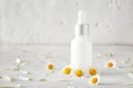 Bottle of cosmetic product with chamomile flowers on light table