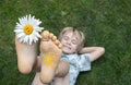 Chamomile flower between toes of bare foot of happy child lying on grass Royalty Free Stock Photo