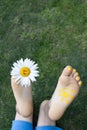 Chamomile flower between toes of bare foot and painted sun on other foot of child lying on grass Royalty Free Stock Photo