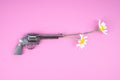 Chamomile flowers placed into the barrel of a revolver on a pink background. Flower power concept