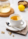 Chamomile herbal tea with lemon in a white cup and teapot with flowers on a light background close up. The concept of a healthy
