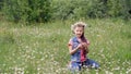 On a chamomile lawn, a sweet girl in a wreath of chamomiles, looks at the daisy, cuts off the petals, sniffs it, and Royalty Free Stock Photo