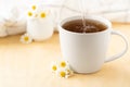 Chamomile tea with kitchen towel and chamomile in white ceramic cup on the wooden table. Herbal tea. Side view Royalty Free Stock Photo