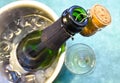 a champagne bottle in a cold bucket with ice and water, the cork holding from the mouth decorating the scene and a cup with Royalty Free Stock Photo