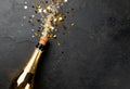 Champagne bottle popping cork with golden confetti and bubbles exploding on a dark textured background for celebration Royalty Free Stock Photo