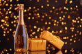 Champagne bottle and wrapped gift on blurred background of Christmas lights Royalty Free Stock Photo