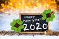 Champagne cork and blackboard with greeting happy new year 2020 wooden planks front of bright golden warm bokeh light background Royalty Free Stock Photo