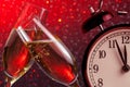 Champagne flutes with golden bubbles on christmas red light bokeh background with vintage alarm clock Royalty Free Stock Photo