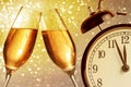 Champagne flutes with golden bubbles on golden light bokeh background with vintage alarm clock Royalty Free Stock Photo