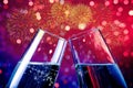 Champagne flutes with golden bubbles on red and purple light bokeh and fireworks sparkle background