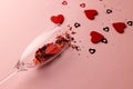 Champagne glass spilling red heart shapes and confetti on pale pink background with copy space