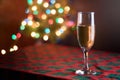 Champagne glass on table with blurred Christmas tree and lights in the background. Christmas background with beautiful bokeh and Royalty Free Stock Photo