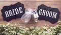 Champagne glass in wedding dress with Bride and Groom text sign on wooden background decorated with tiny white flower, vintage