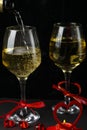 Champagne is poured into glasses tied with a ribbon on a black background next to a heart a candlestick with a burning candle