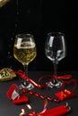 Champagne is poured into glasses tied with a ribbon on a black background, next to a heart, a candlestick with a burning