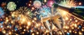 Champagne pouring into glass flutes from a bottle over colorful fireworks and glittering lights background.