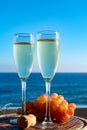 Champagne, prosecco or cava served with pink grape in two glasses on outside terrace with sea view