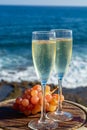 Champagne, prosecco or cava served with pink grape in two glasses on outside terrace with sea view